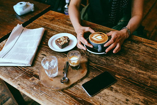 Vintage low key image of a coffee on the table in a cafe in East London. Young woman is having a cappuccino and some sweets, a delicious chocolate cake.