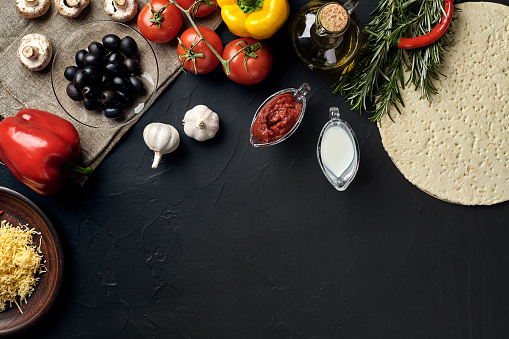 Pizza cooking ingredients. Dough, vegetables and spices on black background. Top view with copy space. Still life. Flat lay