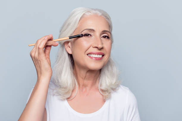 istock Nice, delighted, caucasian, attractive, aged woman applying eyeshadow, using tassel, making, doing professional make up over grey background 925942082