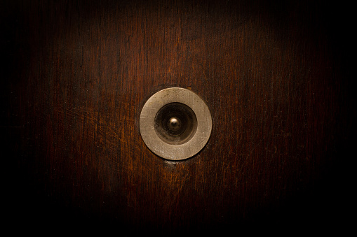 front view closeup of vintage metallic view finder on blown scratched wooden door texture