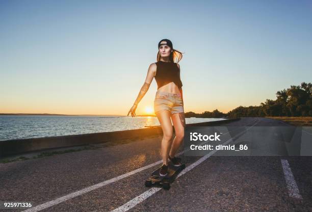 A Beautiful Sexy Blond Hipster With Blue Hair In A Tattoo Is Riding A Longboard Stock Photo - Download Image Now