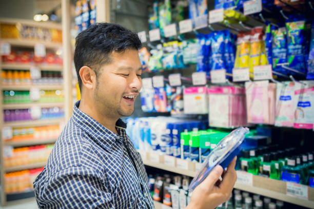 schöner asiatischer mann im supermarkt einkaufen.  rasierer zu wählen und suchen es - disaffection stock-fotos und bilder
