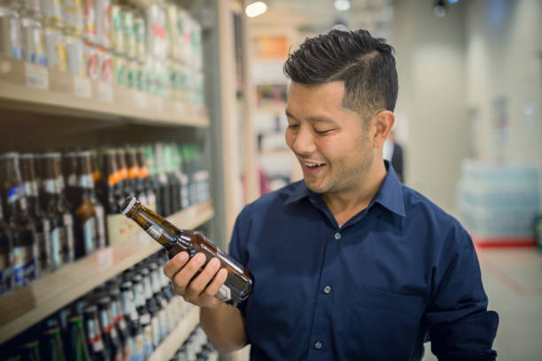 bel giovane asiatico felice di selezionare una birra dal supermercato. - bottling plant brewery industry food foto e immagini stock