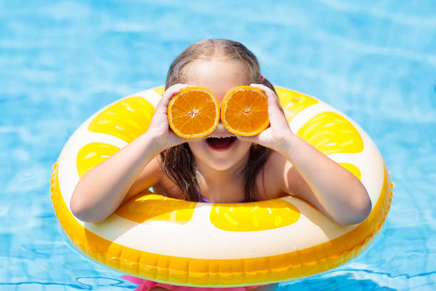 istock Child in swimming pool. Kid eating orange. 925984584
