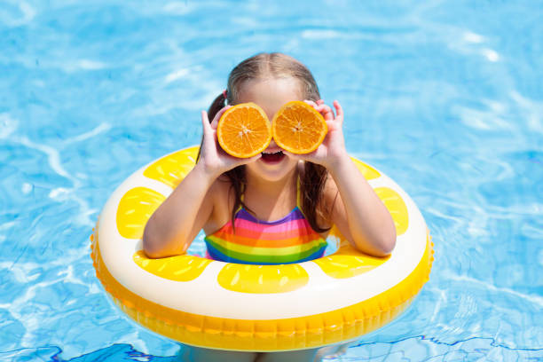 istock Child in swimming pool. Kid eating orange. 925987732