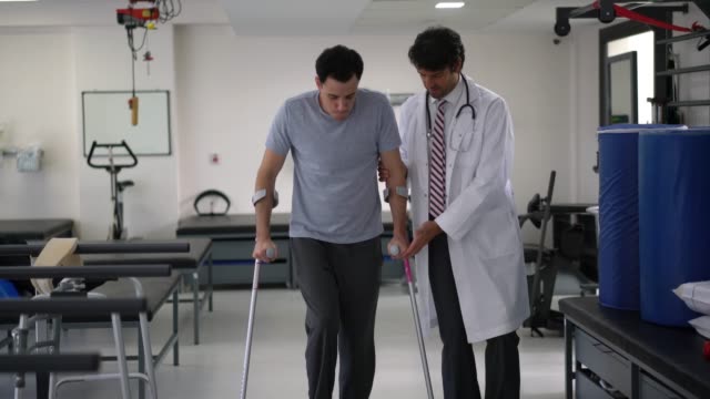Orthopedist at the hospital helping a young patient use crutches for the first time
