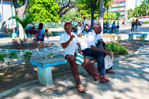 Santiago de Cuba, Cuba, January 5th 2017Two friends sitting on a bench on a public park in Santiago de Cuba, the man is looking a way and the other looking at the camera smiling