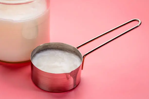 measuring scoop and glass jar of coconut cooking oil on a pink background