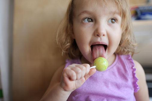 The girl eats big lollipop. The girl licks candy