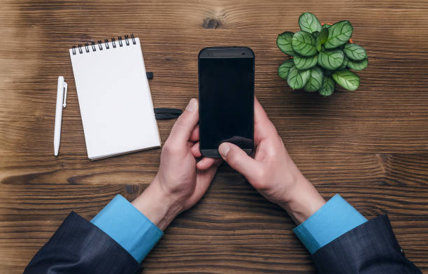 istock Businessman writing a message with mobile phone in his hands. Note pad with blank paper page sheets on offic table. 926062764