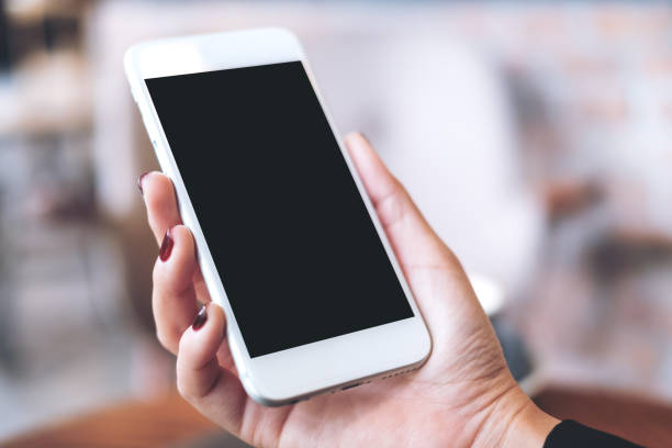 istock Mockup image of a hand holding white mobile phone with blank black desktop screen with blur background 926070014