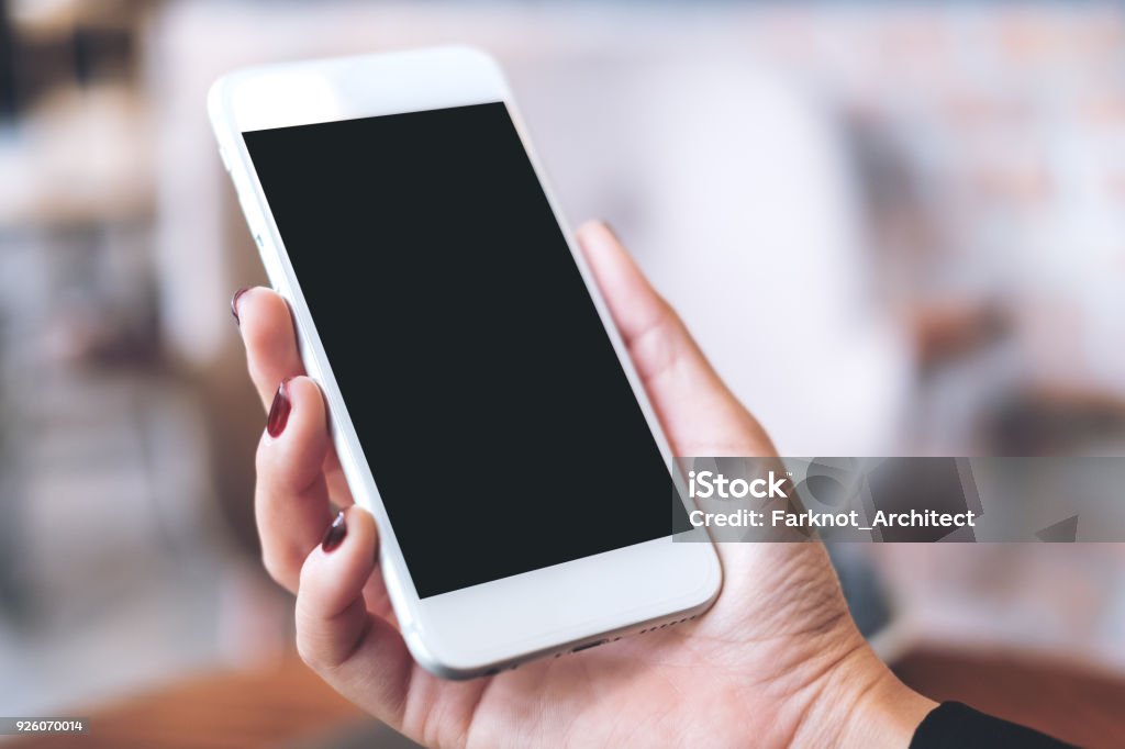 Mockup image of a hand holding white mobile phone with blank black desktop screen with blur background Smart Phone Stock Photo