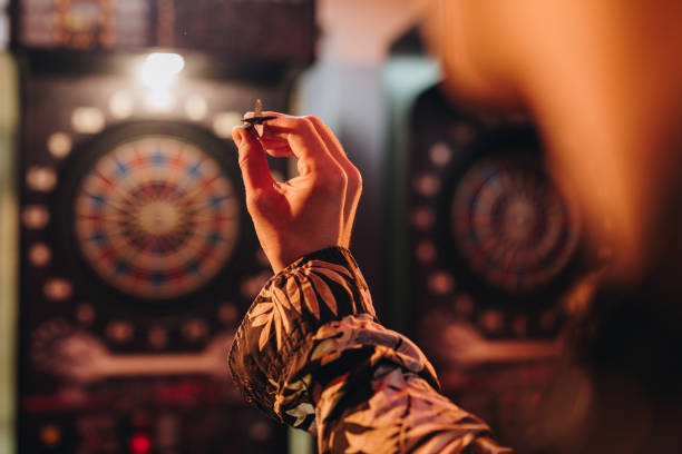 Unrecognizable person aiming at dartboard in a pub. Close up of a man holding dart and aiming while playing darts in entertainment club. darts stock pictures, royalty-free photos & images