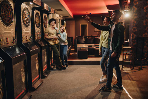 Full length of happy couple playing darts in a bar. Young happy couple having fun with their friends while playing darts in a pub. woman darts stock pictures, royalty-free photos & images