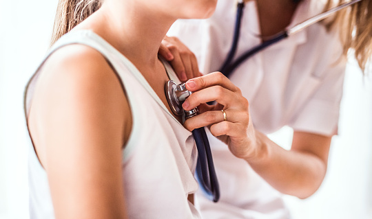 Unrecognizable young female doctor examining a small girl with stethoscope in her office. Close up.