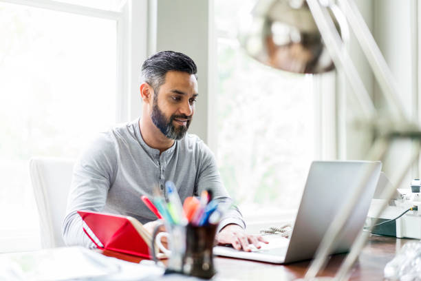 istock Man using laptop at desk in home office 926084702