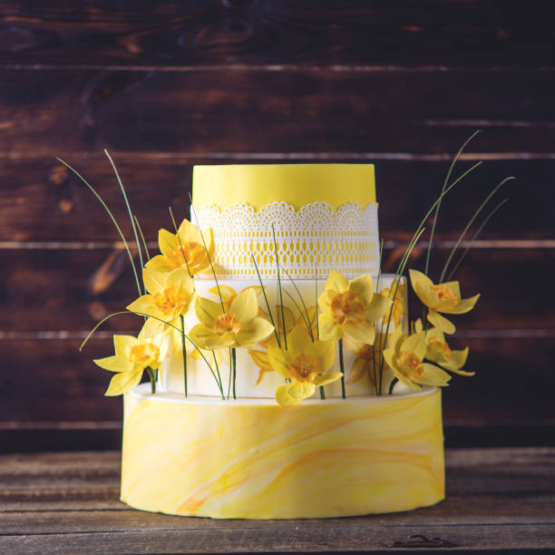 Beautiful home yellow wedding three-tiered cake decorated with red spring flowers. Concept floral trends in desserts stock photo