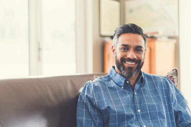 istock Portrait of smiling man sitting on sofa at home 926084880