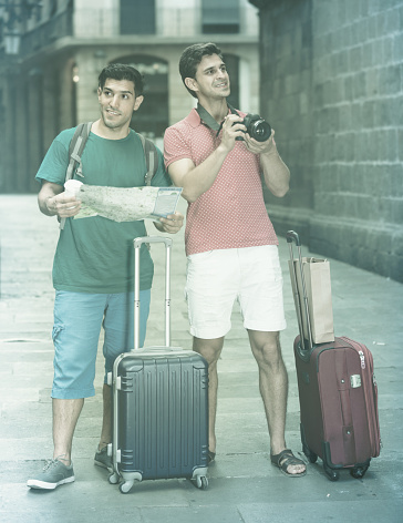 Adult men with suitcases are walking with map and photographing in Barcelona.