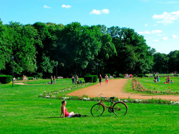Young woman, bicycle, public park, Margaret island, Budapest Hungary, Budapest. Public park on the Margaret island. Young woman sits on green grass and rests. A bicycle is next to her. Other people rests in the park too. Sunny day. margitsziget stock pictures, royalty-free photos & images