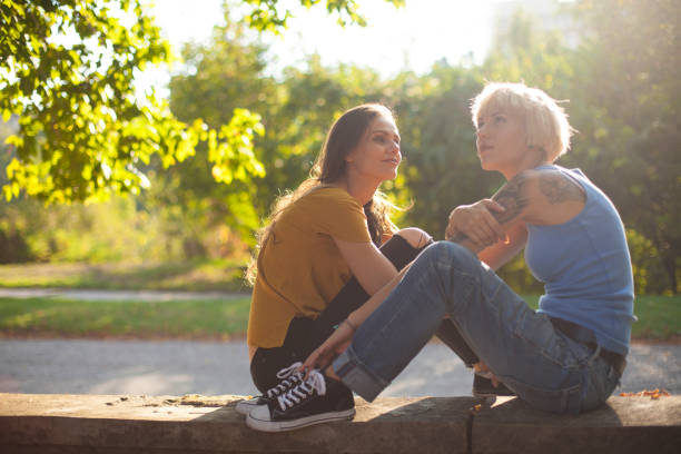 Two girls sitting in park, resting and talking. Both with casual clothes.