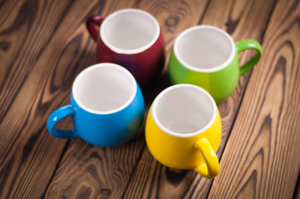 istock Four colored empty ceramic clean mugs on old worn brown wooden table 926143946