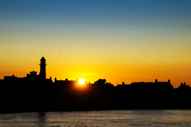 The sun setting over the rooftops at Gorleston-on-Sea in Norfolk, Eastern England, with buildings and the old lighthouse in silhouette. Gorleston-on-Sea is a town beside the River Yare, across the river from its larger neighbour Great Yarmouth.