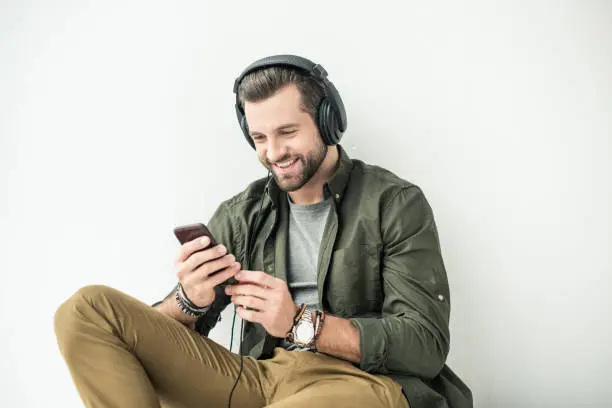Photo of handsome smiling man listening music with smartphone isolated on white