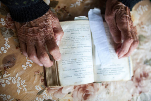 istock Old woman hands on the open prayer book. 926163338