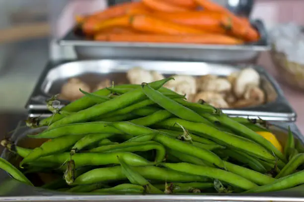 Fresh vegetables in a metal trays in the restaurant. Carrots, green string beans, champignons