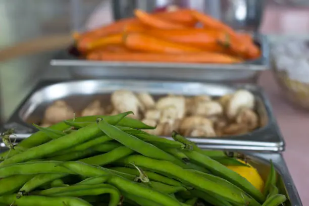 Fresh vegetables in a metal trays in the restaurant. Carrots, green string beans, champignons