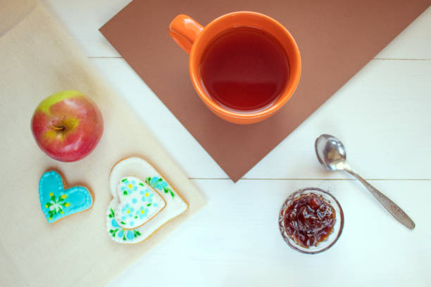 Dinner is a dessert on the table which consists of tea in a cup and biscuits with jam. There is a red apple