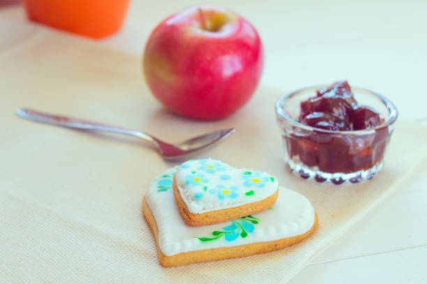 Dinner is a dessert on the table which consists of tea in a cup and biscuits with jam. There is a red apple