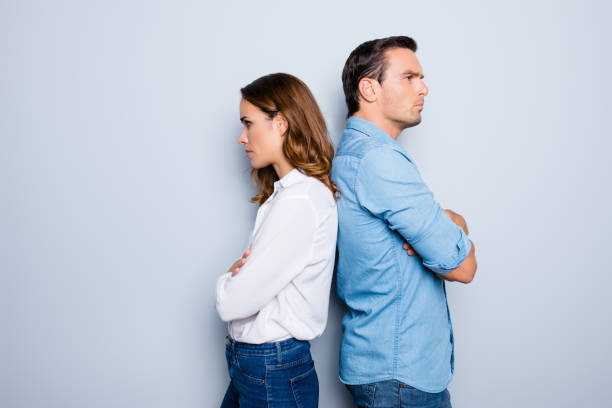 ritratto di coppia frustrata infelice in piedi da un paese all'altro che non parla tra loro dopo una discussione mentre si trova su sfondo grigio. reazione di espressione facciale dell'emozione negativa - arguing anger couple furious foto e immagini stock