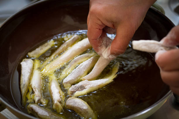 Italian Cuisine: Hands Putting Small Fish to Fry in Pan stock photo