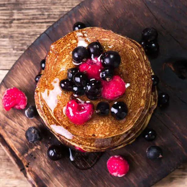 Photo of Buckwheat pancakes with berry fruit and honey on wooden vintage table