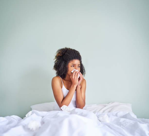 I hate getting sick when I have to go to work Shot of a uncomfortable looking young woman holding her nose with a tissue after waking up from sleeping in her bed cold virus stock pictures, royalty-free photos & images