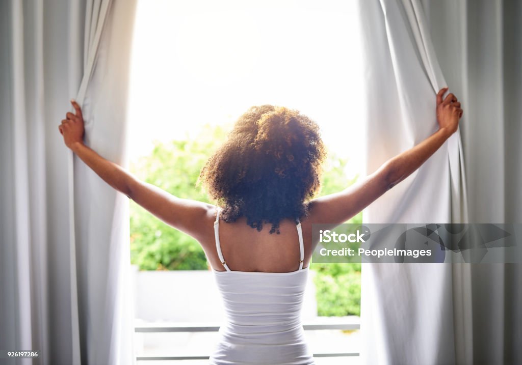 Good morning world! Rearview shot of an unrecognizable woman opening her bedroom curtains after waking up from sleeping Window Stock Photo