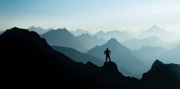 Spectacular mountain ranges silhouettes. Man reaching summit enjoying freedom. stock photo