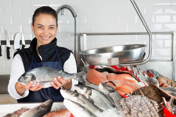 Woman Selling Fish Woman is showing a fish to camera  with a toothy smile. fish market photos stock pictures, royalty-free photos & images