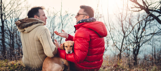 coppia gay maschile con cane seduto sull'erba all'aperto - alternative health care foto e immagini stock