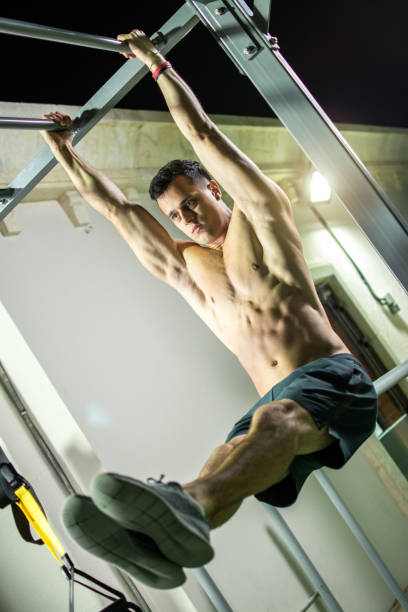 istock Handsome shirtless man doing pull ups in the L-sit position on horizontal bar outdoors at night. Calisthenics training. 926228014