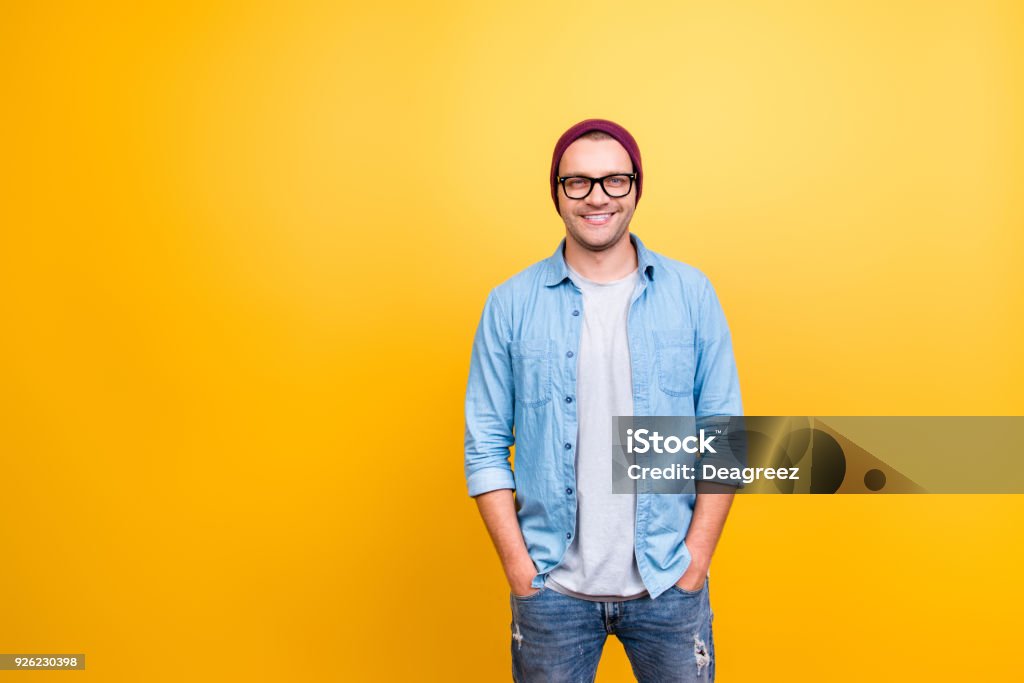 Retrato con espacio de copia de sonriente, feliz chico en desgaste los pantalones vaqueros, gafas, gorra roja cogidos de la mano en el bolsillo, mirando a cámara sobre fondo amarillo - Foto de stock de Hombres libre de derechos