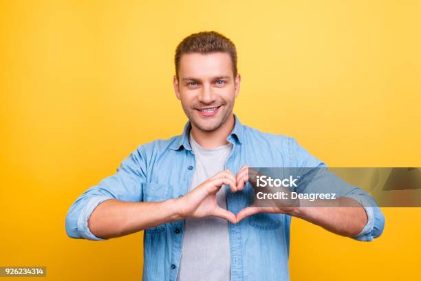 Portrait Of Smiling Stunning Man With Stubble Showing Heart Figure With Fingers Over Yellow Background Stock Photo - Download Image Now