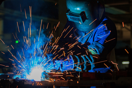 Industrial worker is welding metal part in factory