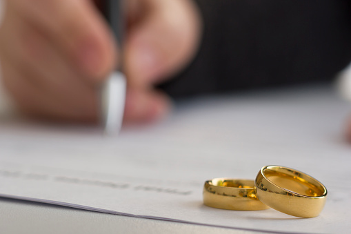 Hands of wife, husband signing decree of divorce, dissolution, canceling marriage, legal separation documents, filing divorce papers or premarital agreement prepared by lawyer. Wedding ring.