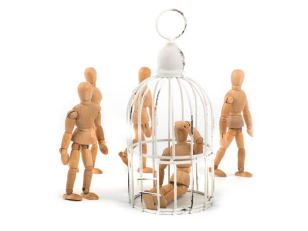 istock Wooden mannequin sits in cage in crowd - depression? helpless? ignorance? 926243014