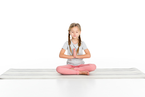 kid sitting in lotus position on yoga mat isolated on white