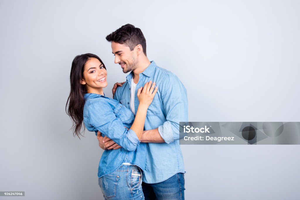 Portrait of sweet hispanic cute lovers, bearded man hugging woman and looking at her, pretty woman looking at camera over grey background Couple - Relationship Stock Photo