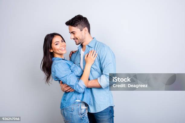 Portrait Of Sweet Hispanic Cute Lovers Bearded Man Hugging Woman And Looking At Her Pretty Woman Looking At Camera Over Grey Background Stock Photo - Download Image Now